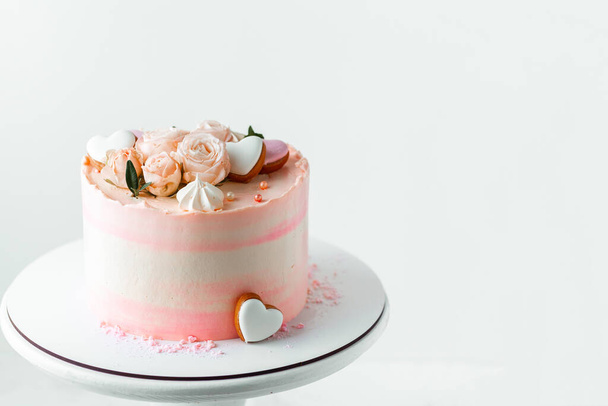 Pastel rosado decorado con flores rosadas y galletas de merengue en el fondo blanco. Feliz pastel de San Valentín. Pastel rosa de boda en el soporte de pastel blanco - Foto, Imagen