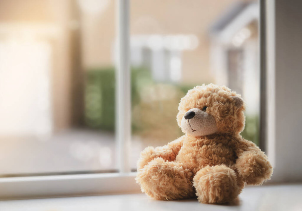 Высокий ключевой свет грустный плюшевый медведь сидит рядом с окном солнечный день, одинокий коричневый медведь сидит один дома, Концепция социального дистанцирования, остаться дома и предотвратить распространение вируса и болезней у детей - Фото, изображение