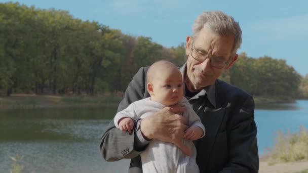 Abuelo sosteniendo al bebé en brazos afuera. Vinculación de los abuelos con los nietos. - Imágenes, Vídeo