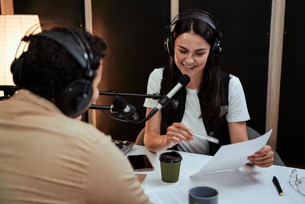 Портал счастливой женщины-радиоведущей, улыбающейся, читающей сценарий из бумаги во время разговора с гостем-мужчиной, ведущей, ведущей живого шоу в студии - Фото, изображение