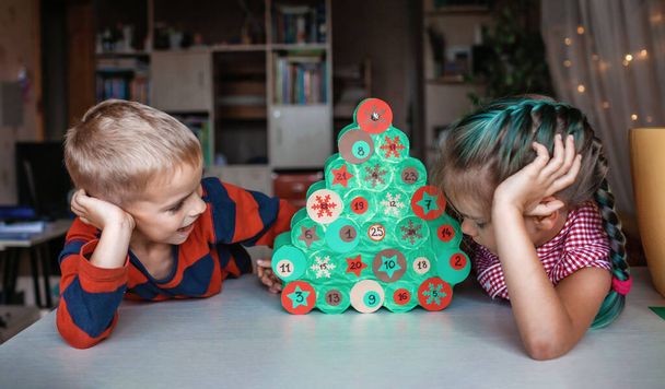 Cute little kid making handmade advent calendar with toilet paper rolls at home. Glue, colored paper, cut punch to hide sweets and candies in rolls. Seasonal activity for kids, family winter holidays - Photo, Image