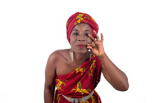 Красивая африканская женщина в традиционной одежде, смотрит в камеру и делает жест рукой изолирован на белом фоне - Фото, изображение