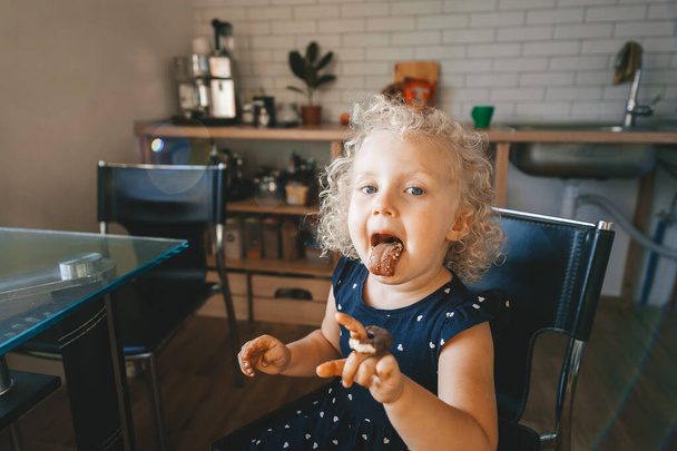 Cute little blonde girl shows tongue like Einstein and is eating chocolate cookies. Closeup portrait. - Fotografie, Obrázek