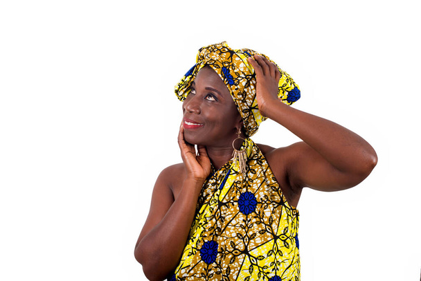 jonge Afrikaanse vrouw staat in lendendoek in een studio en kijkt naar boven glimlachend. - Foto, afbeelding
