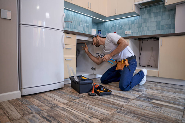 młody biały mężczyzna pracownik instalowanie umywalka za pomocą klucza - Zdjęcie, obraz
