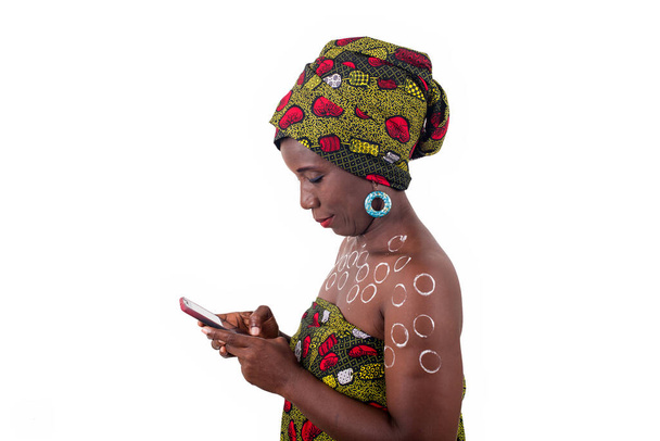jovem mulher africana de pé em tecido de lantejoulas em um estúdio olhando para o telefone móvel enquanto sorri. - Foto, Imagem