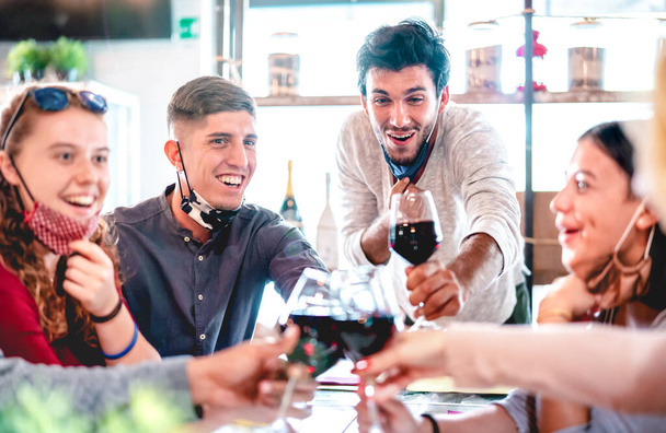 Друзья пьют вино в ресторане в масках для лица - Новая концепция нормального образа жизни со счастливыми людьми, веселящимися вместе в винном баре - Яркий фильтр подсветки с акцентом на среднего правого парня - Фото, изображение