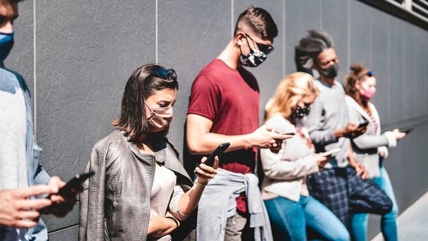 フェイスマスクで覆われた携帯電話を使用している人々のサイドビュー-スマートフォンでコンテンツを共有する若い友人-常に接続されたティーンエイジャーと新しい通常のライフスタイルコンセプト-暖かい鮮やかなフィルター - 写真・画像