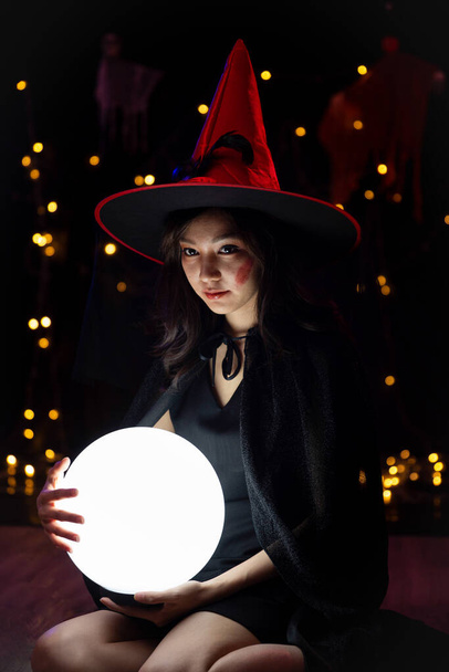 Una donna che indossa un costume da strega e tiene una sfera di cristallo ad Halloween. Festival di Halloween. - Foto, immagini