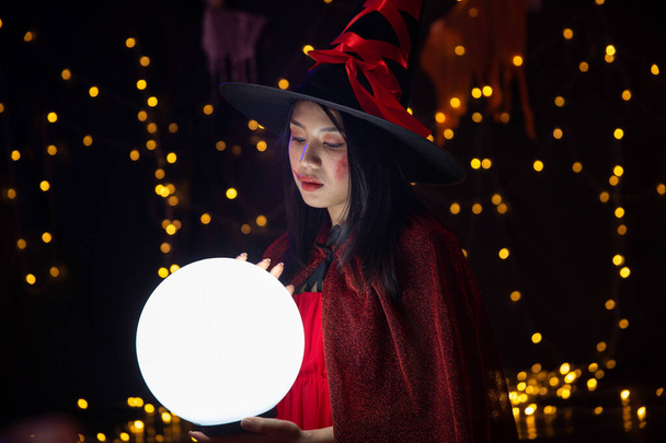 Μια γυναίκα που φοράει στολή μάγισσας και κρατάει μια κρυστάλλινη σφαίρα στο Χάλογουιν. Φεστιβάλ Halloween. - Φωτογραφία, εικόνα