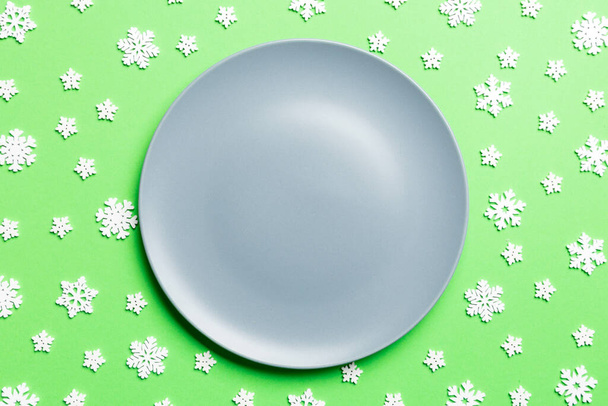 Horní pohled na prázdný talíř obklopený sněhovými vločkami na barevném pozadí. Nový rok večeře koncept. - Fotografie, Obrázek