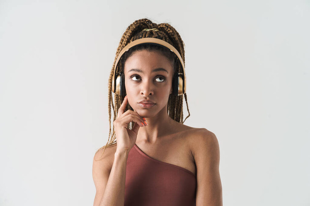 Portrait of beautiful pensive african brunette woman with dreadlocks a listening music via wireless headphones isolated on white background - Foto, Imagem