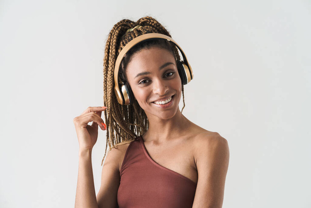 Portrait of beautiful smiling african brunette woman with dreadlocks a listening music via wireless headphones isolated on white background - 写真・画像