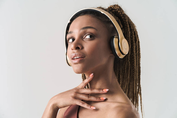 Close up portrait of beautiful african brunette woman with dreadlocks a listening music via wireless headphones isolated on white background - Foto, Imagen