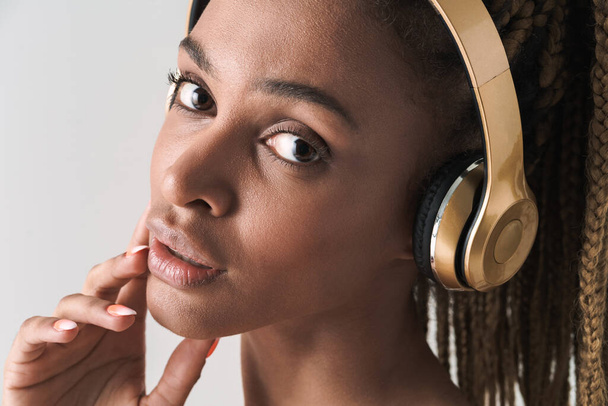 Close up portrait of beautiful african brunette woman with dreadlocks a listening music via wireless headphones isolated on white background - Φωτογραφία, εικόνα