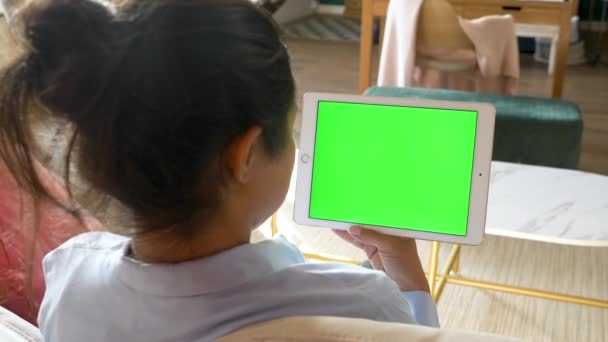 Una giovane donna indiana tiene in mano utilizza una tavoletta con uno schermo verde Chromakey funziona online in una stanza luminosa a casa - Filmati, video