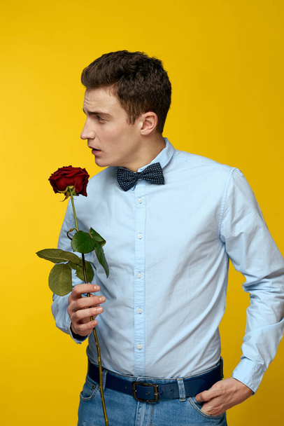 Elegant man in a suit with a red rose in his hands on a yellow background, cropped view - Фото, зображення