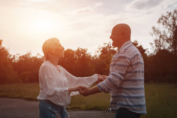gelukkig senior paar dating, knuffelen en zoenen buiten bij zonsondergang - Foto, afbeelding