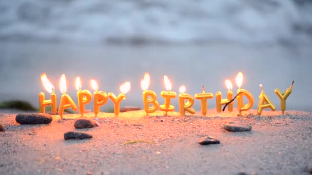 Palabra de velas feliz cumpleaños ardiendo en la arena en la playa de arena - Metraje, vídeo