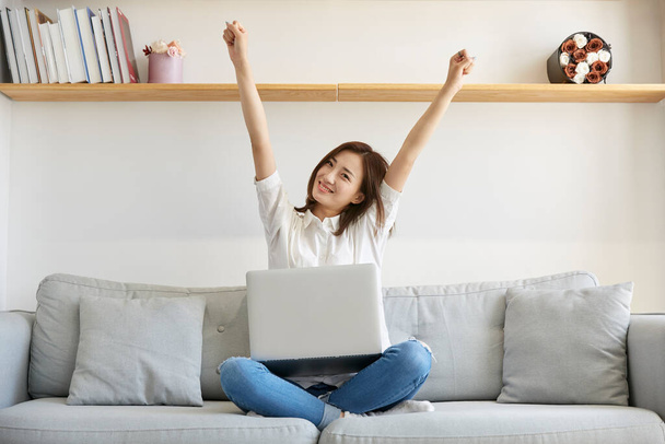 young asian business woman working from home sitting on couch stretching arms happy and smiling - Photo, Image