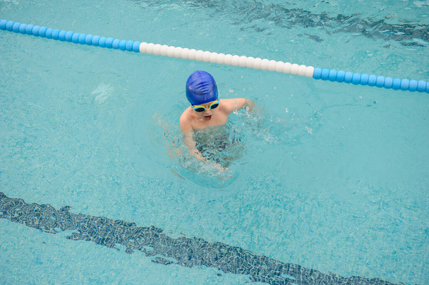 κορυφαία άποψη ενός επτάχρονου αγοριού που παίζει και κολυμπάει στην πισίνα - Φωτογραφία, εικόνα