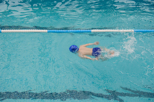 vista superior de un niño de 7 años jugando y nadando en la piscina - Foto, imagen