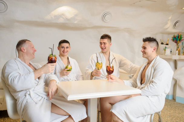 close up photo of 4 men in white gowns sitting around a table and drinking sangria and limonade - Photo, Image