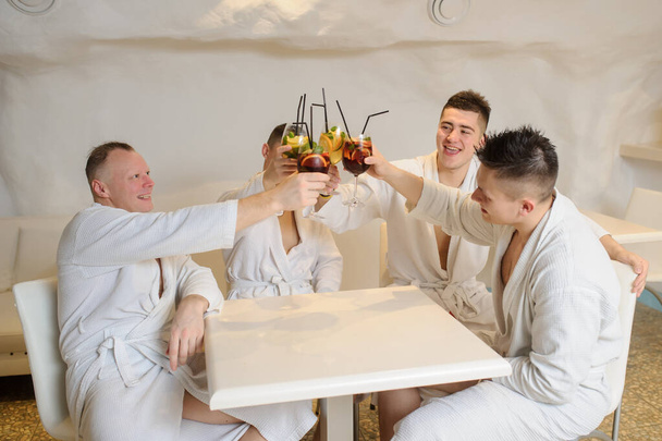 close up photo of 4 men in white gowns sitting around a table and drinking sangria and limonade - Photo, Image