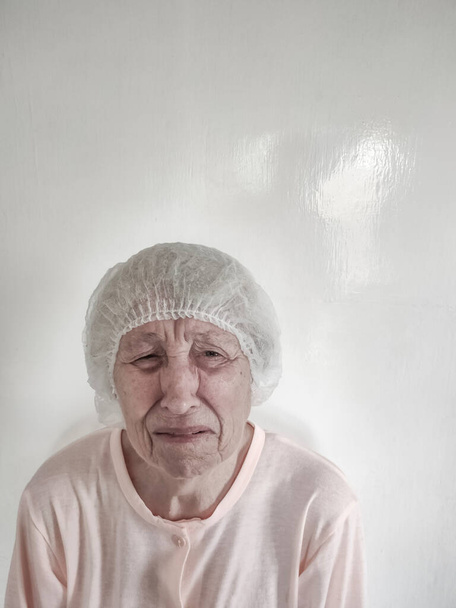 Medikal şapkalı, ağlayan yaşlı bir kadın. Salgın koronavirüs. İnsan sağlığı. Salgın covid-19. Başhekim umutsuzluğa düştü.. - Fotoğraf, Görsel