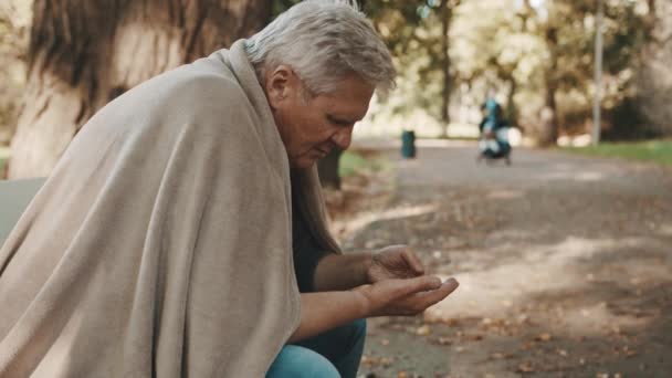 Arme, oudere dakloze man die op herfstdag munten in het park telde. - Video