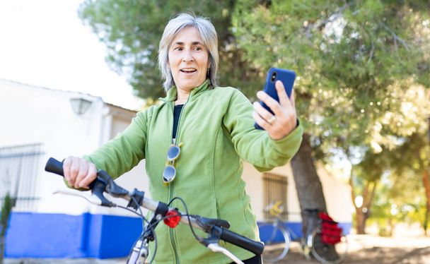 Nainen, jolla on pyörä, katsoo matkapuhelintaan yllättyneellä naamalla - Valokuva, kuva