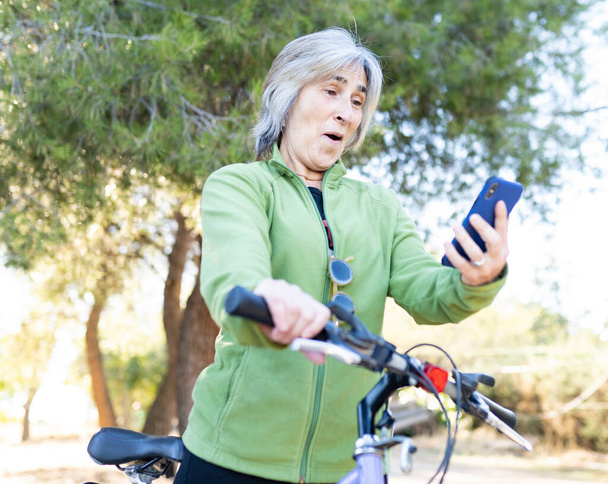 жінка з велосипедом дивиться на свій мобільний телефон з здивованим обличчям
 - Фото, зображення