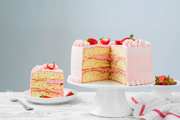 Piękne ciasto warstwowe z różowym maślanym kremem i świeżą truskawką. Kolorowe tło. - Zdjęcie, obraz