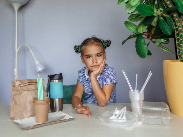 Концепция без пластика и без отходов. Милая девочка-ученица делает выбор между пластиковым и бумажным набором посуды для обеда в школе, зеленой жизни и устойчивого образа жизни - Фото, изображение