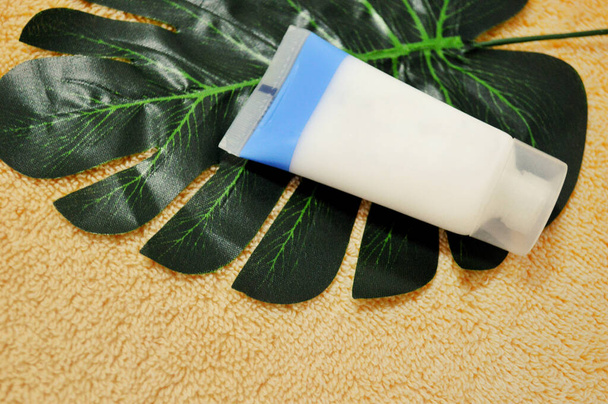 White tube with cream lies on a palm leaf against a background of beige fabric. - Photo, Image