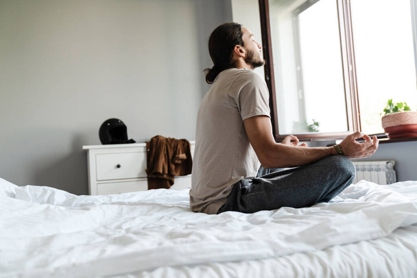 Young man meditating in bedroom in the morning - Photo, image
