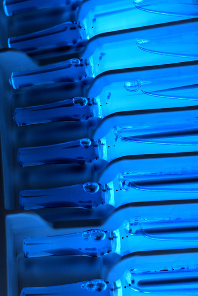 Closeup of row of upright ampules in ultra violet lighting with selective focus - Photo, Image