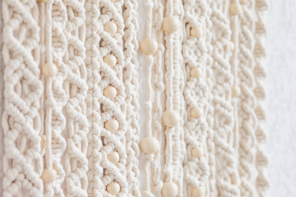 Close-up of hand made macrame texture pattern. Eco friendly modern knitting. Natural decoration concept in the interior. Handmade macrame wall hanging 100% cotton and wooden beads. Soft focus - Foto, afbeelding