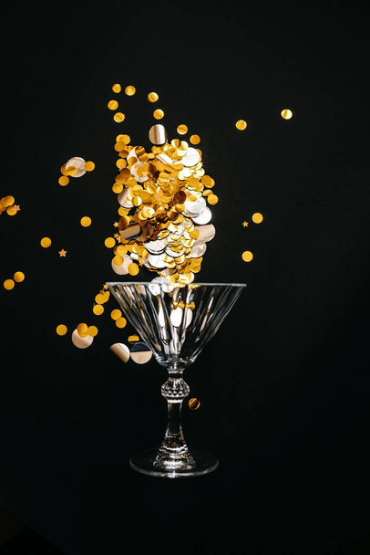 Verre à vin avec des paillettes d'or ou des confettis sur fond noir. Concept de célébration. - Photo, image