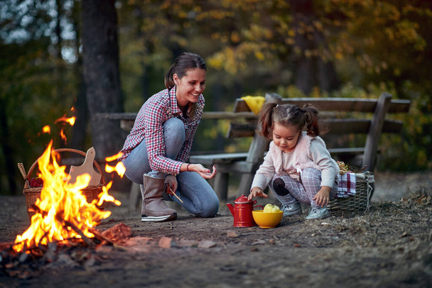 Mother and daughter playing around a campfire in the forest on a beautiful autumn dusk - Foto, imagen