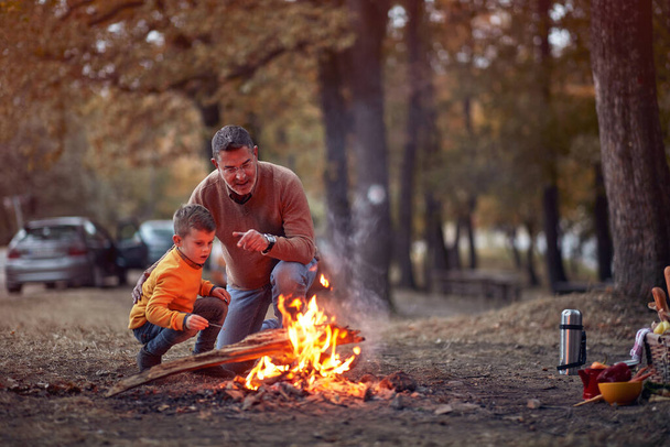 Grandfather and grandson enjoying a campfire in the forest on a beautiful autumn dusk - Foto, imagen