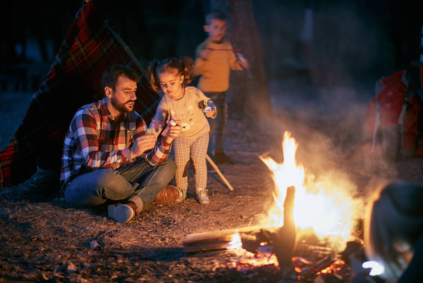 Father and children having a good time around campfire in the forest on a beautiful autumn dusk - Фото, изображение