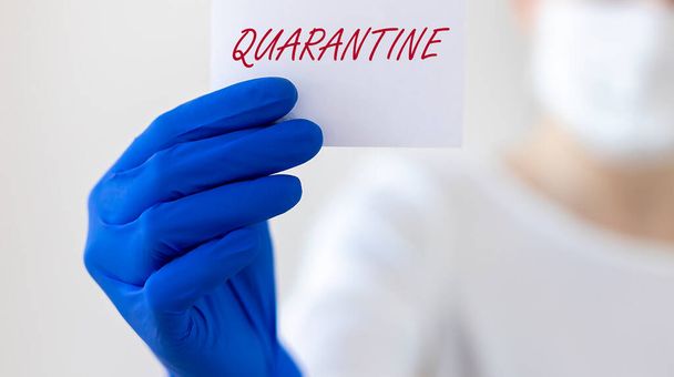 word QUARANTINE on paper in hands of blurred doctor in blue protective gloves, banner - 写真・画像