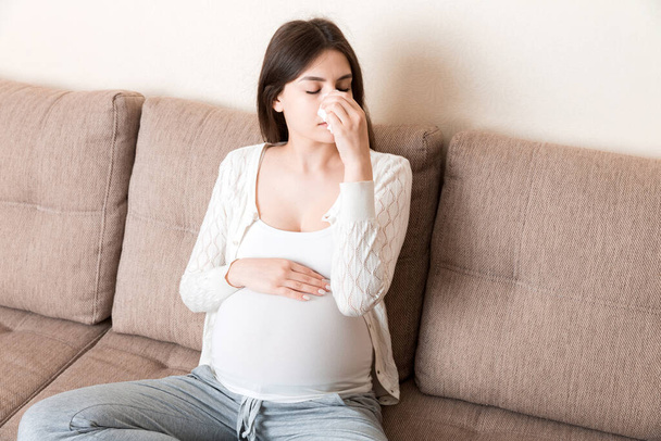 Sick pregnant woman blowing nose into tissue at home Healthy millennial healthcare concept. - Zdjęcie, obraz