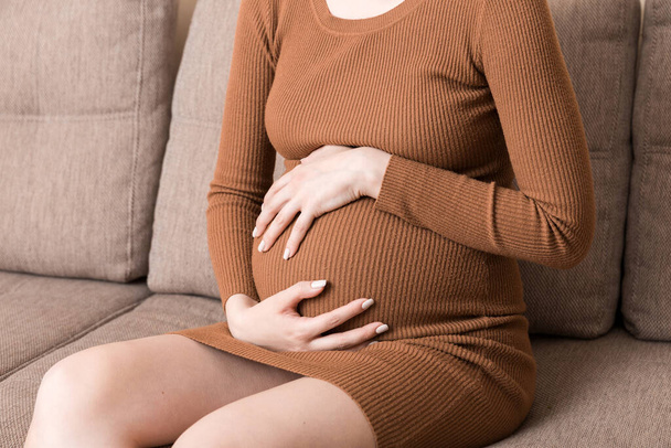 Pregnant Lady Having Massaging Lower belly Sitting On Sofa Indoor. Pregnancy Problems Concept. Maternity healthcare. - Fotoğraf, Görsel