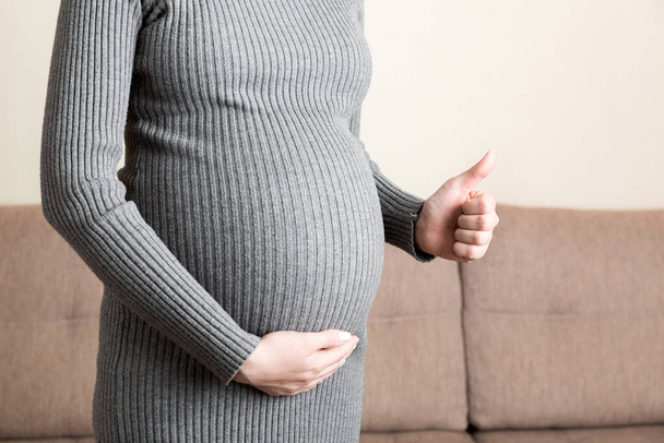 Mujer embarazada mostrando pulgares hacia arriba en la casa. - Foto, Imagen