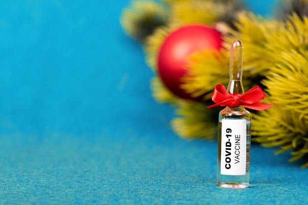 Вакцина COVID-19. Подарок на Новый год. Лучший подарок на Рождество. Новая проверенная вакцина для COVID-19, синий фон, зеленые ветви рождественской елки, рождественский бал. Вид сбоку. Крупный план - Фото, изображение