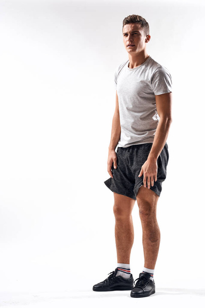 A sports man in shorts and a full-length T-shirt does exercises on a light background - Foto, Imagem