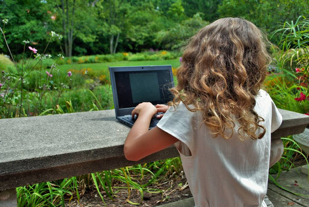 młoda dziewczyna robi pracę w szkole na komputerze zdalnego uczenia się w parku - Zdjęcie, obraz