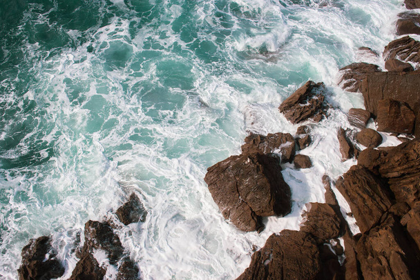 Wellen krachen auf Felsen, Atlantik. Azurblaue Meereswellen mit weißem Schaum brechen an der Küste auf. Spritzer Aquamarin-Meerwasser. Landschaftlich plätschernde Wellen. Erstaunliche Meereslandschaft. Wasser in Bewegung. Meerestapete. - Foto, Bild